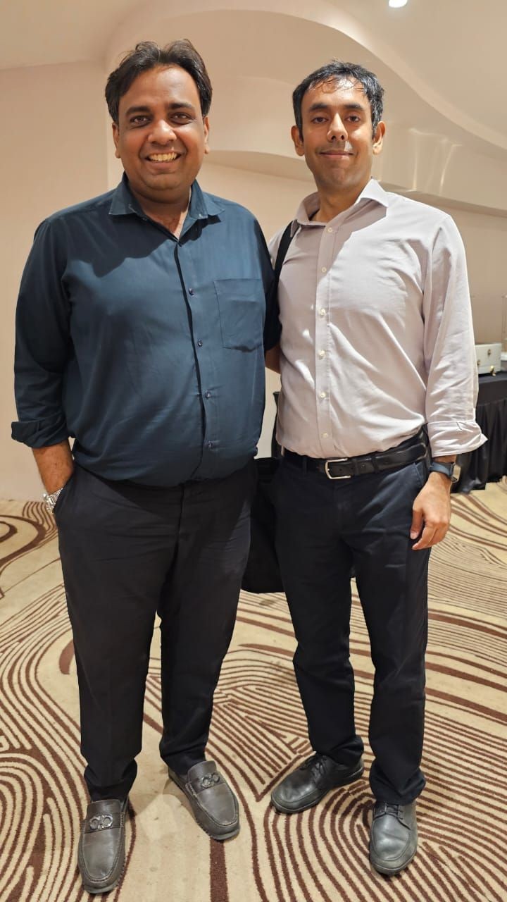 Two men smiling and standing in a conference room, wearing smart casual attire.